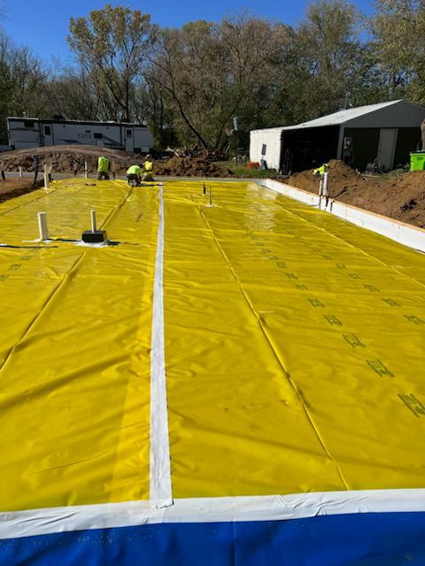Large yellow waterproof liner spread over a backyard construction site with workers in the distance