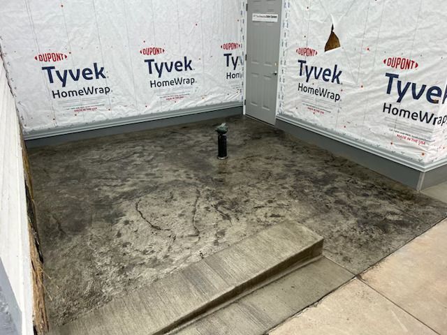 Concrete slab under construction wrapped in Tyvek HomeWrap, with a small black pipe protruding from the floor