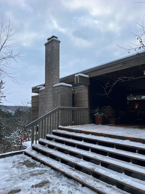 Snow-dusted front steps leading to a brick house with a tall chimney and open garage during winter
