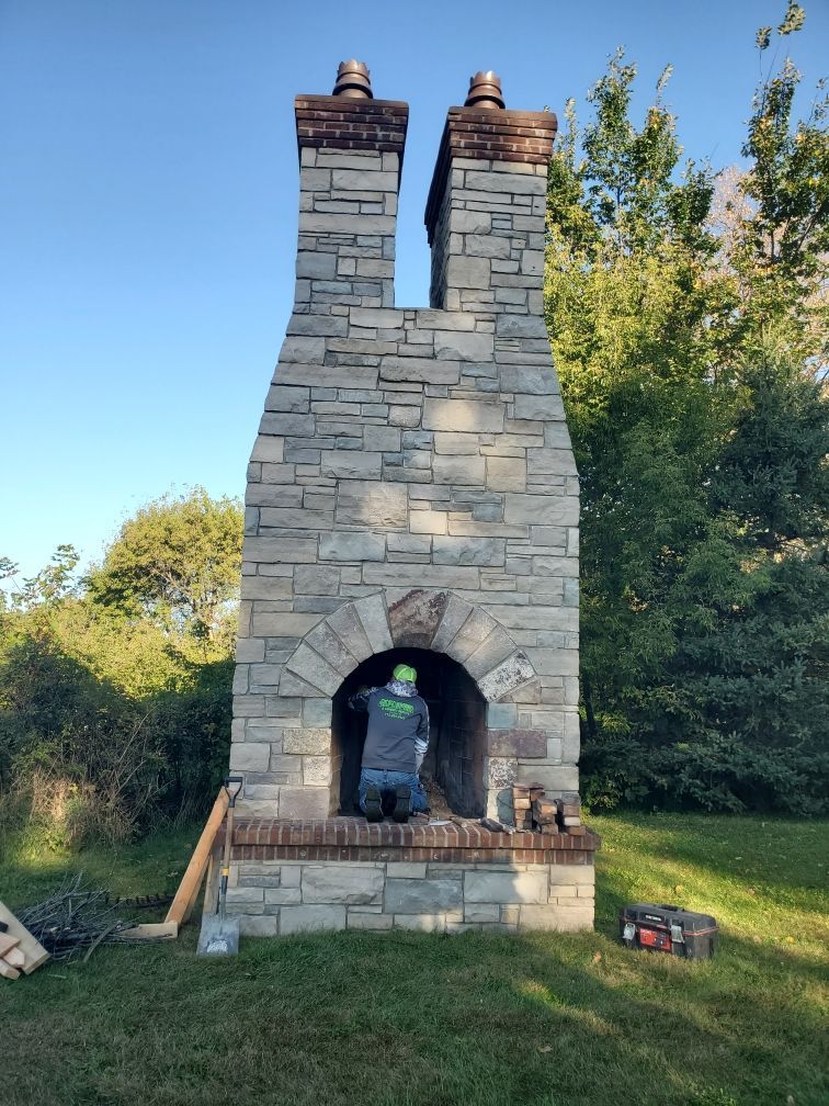 Stone outdoor fireplace with tall twin chimneys and arched firebox in a grassy yard