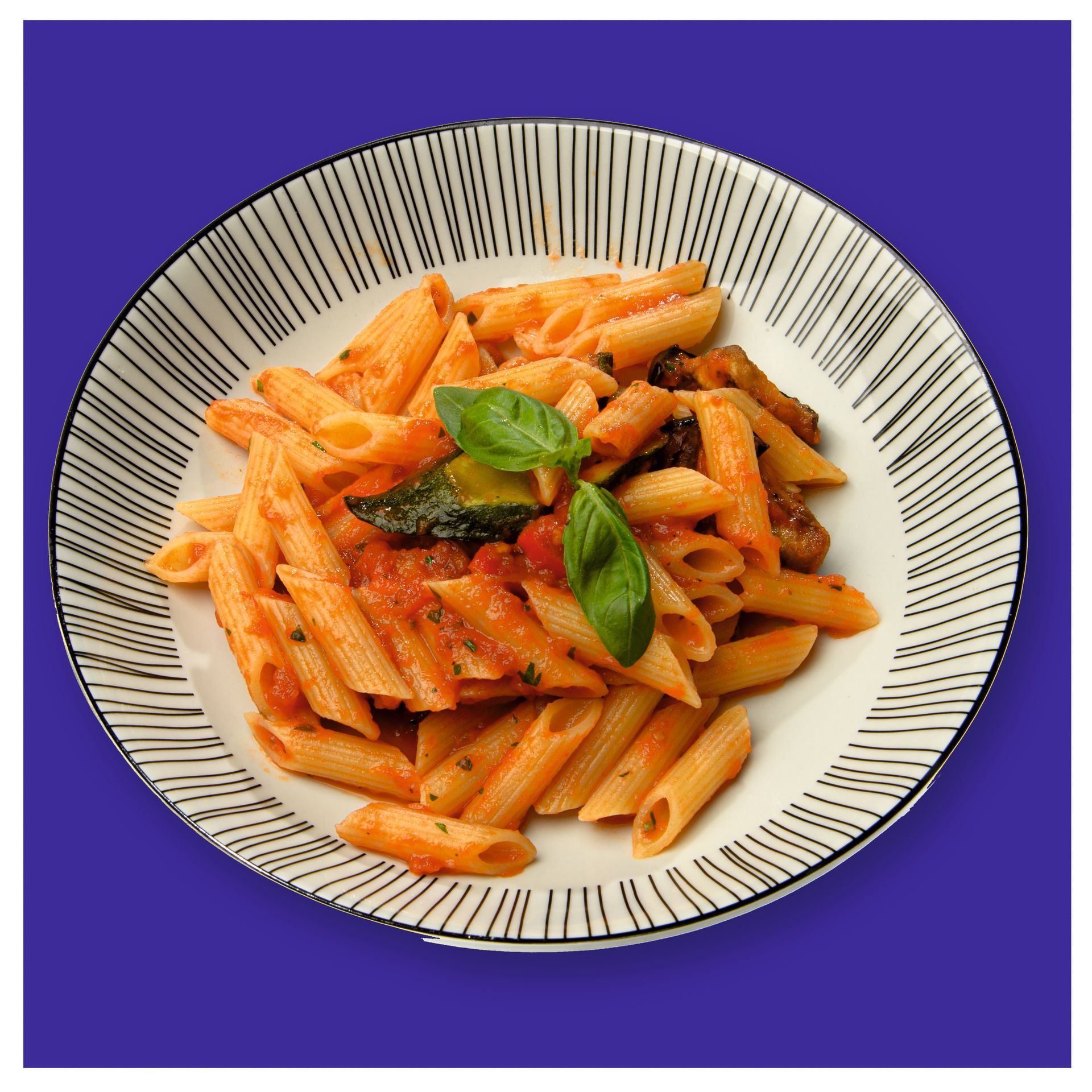 Un piatto di pasta con sugo di pomodoro e basilico su sfondo blu.