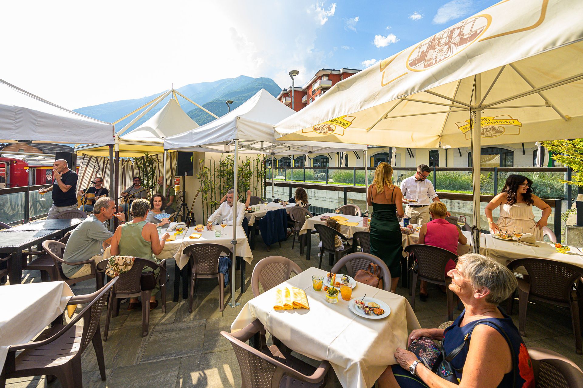 Un gruppo di persone è seduto ai tavoli di un ristorante sotto gli ombrelloni.