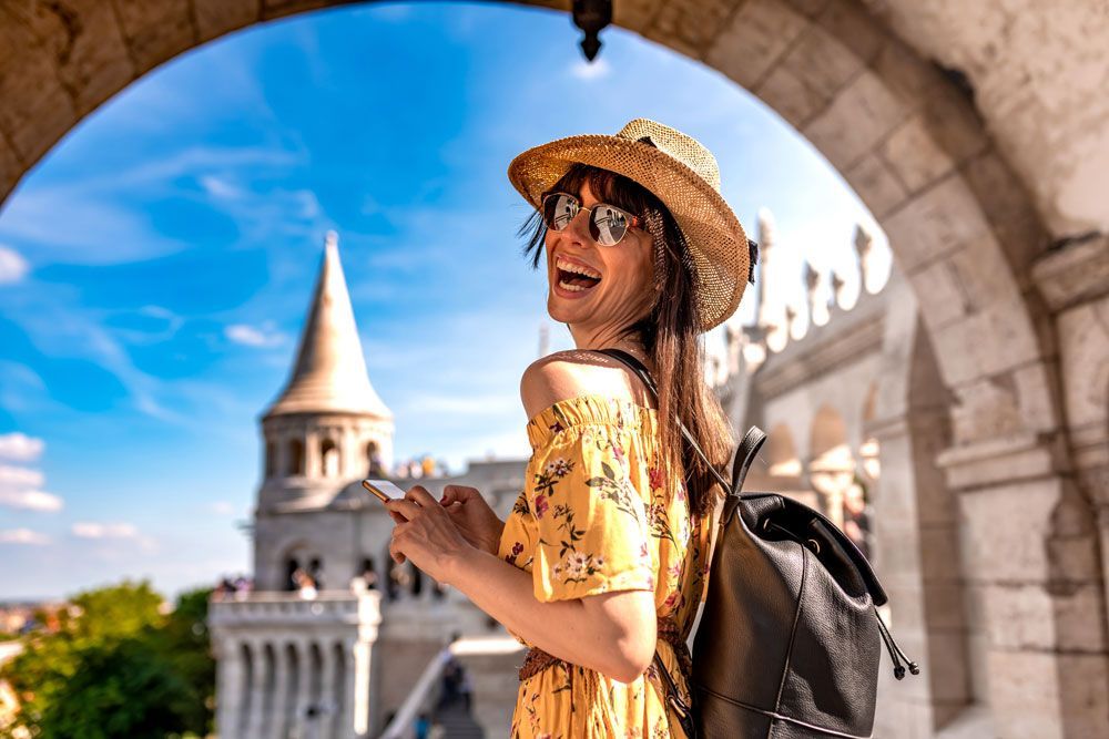 Woman in yellow dress and straw hat in an archway, looking back toward a stone tower under a bright blue sky