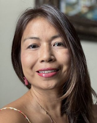 Woman with long dark hair, wearing a necklace and pink earrings, smiling at the camera.