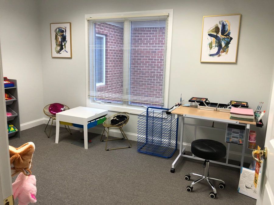 A room with a desk , chairs , a table and a window.