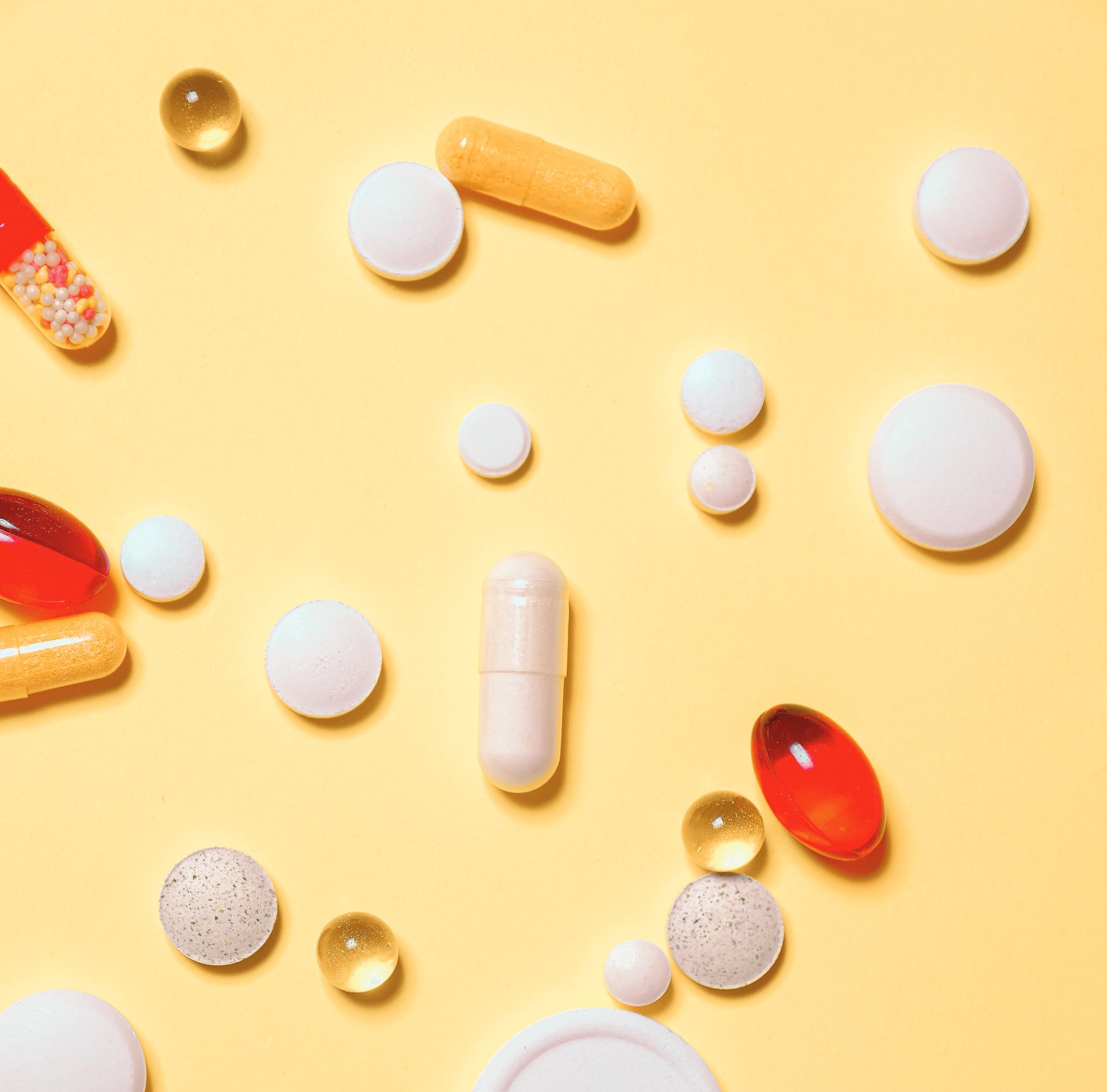 Scattered assorted pills and capsules on a yellow background