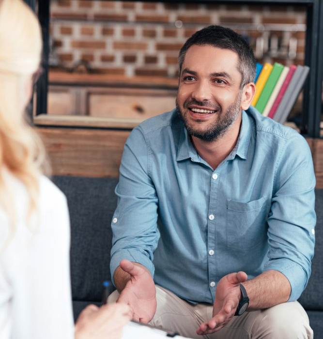 Smiling man in a blue shirt talking with someone across the table in a cozy office setting