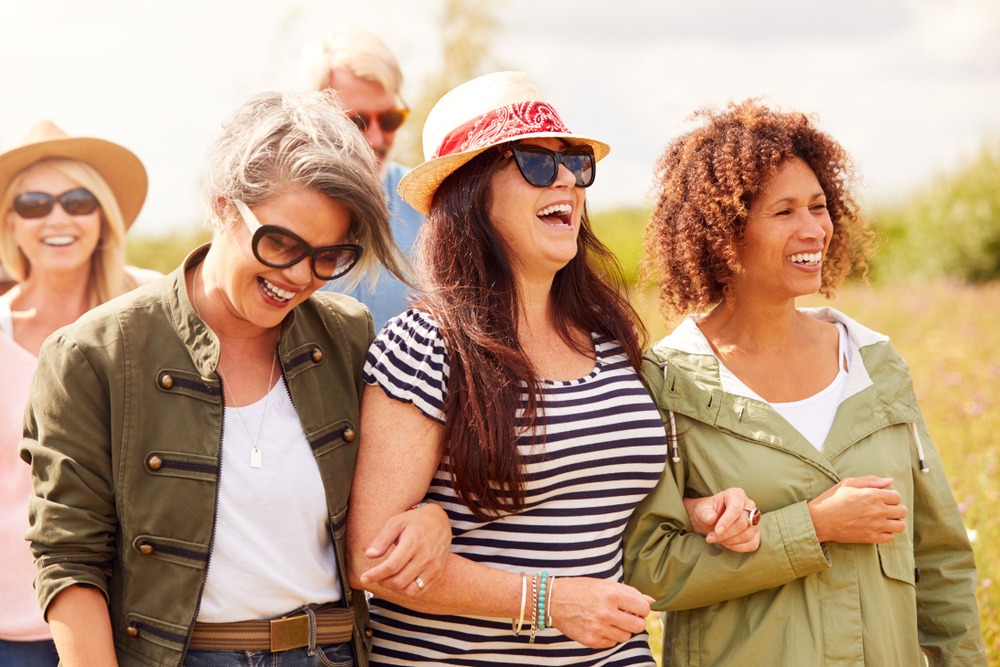 Four smiling friends walking outdoors in sunglasses and summer clothing