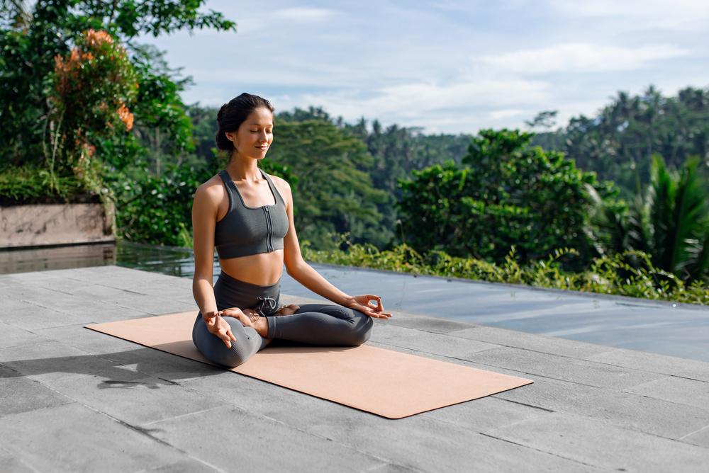 Person meditating on a mat outdoors on a rooftop with greenery in the background