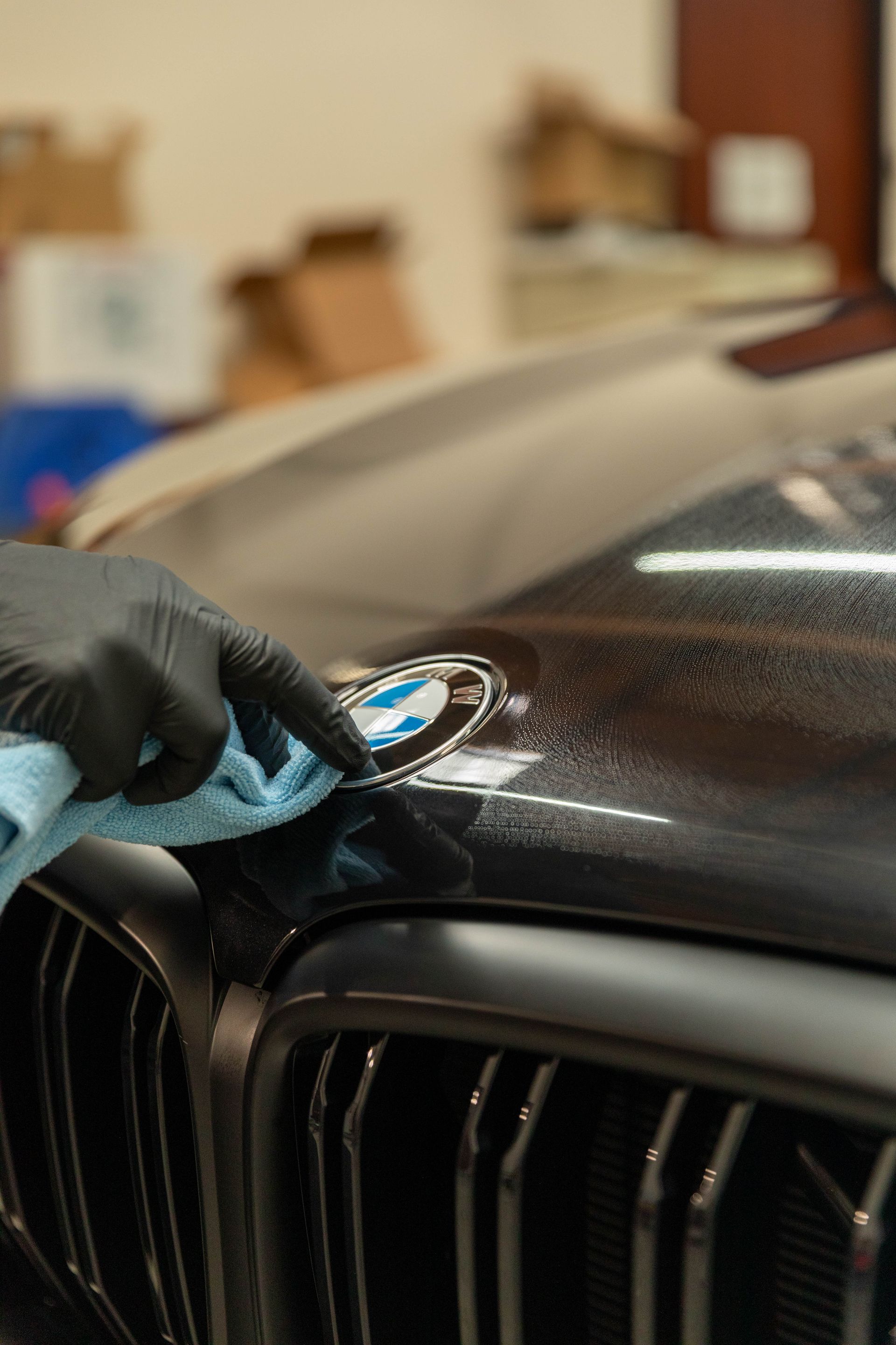 Gloved hand polishing a black car hood near the grille with a microfiber cloth