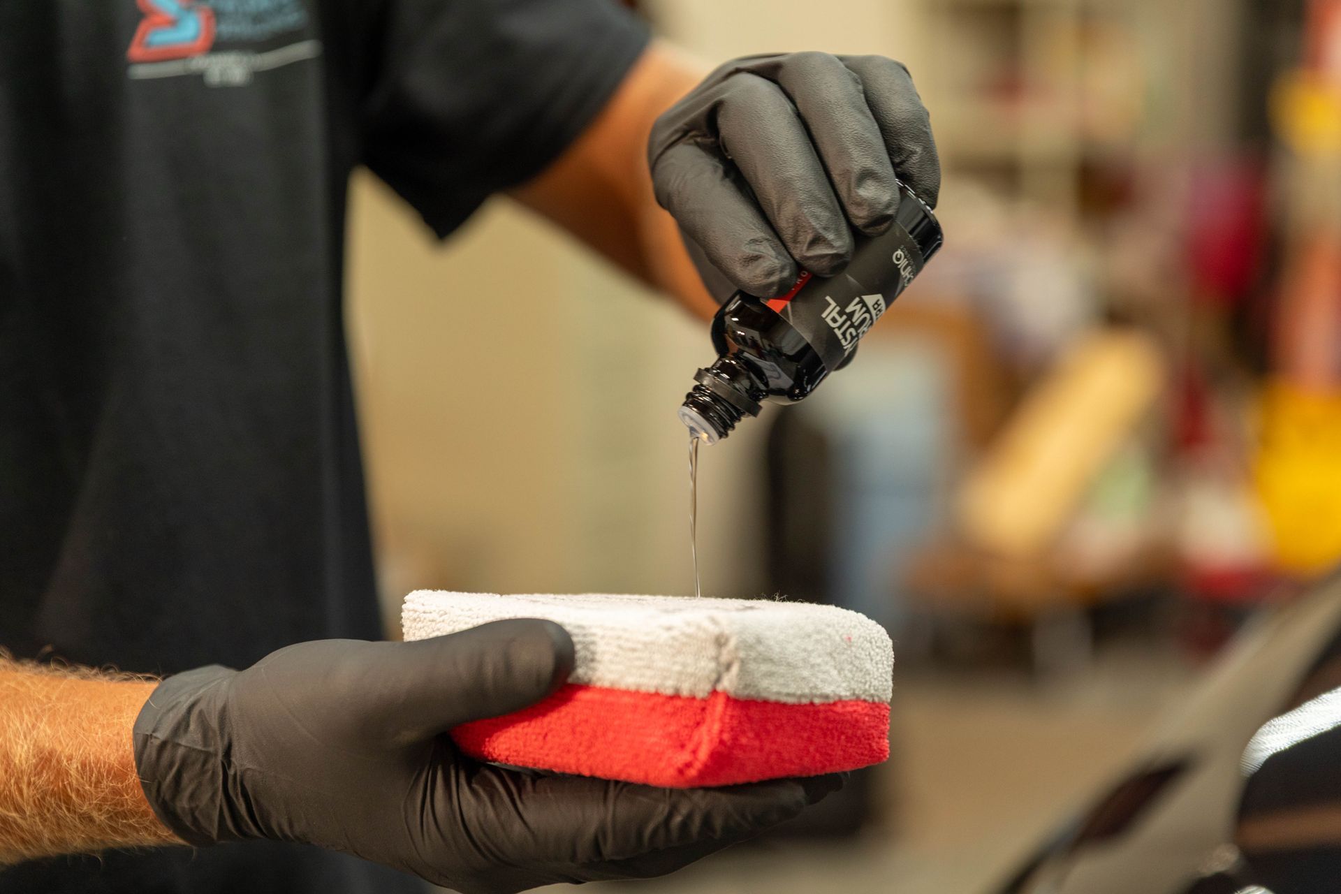 Gloved hands applying adhesive to a red and white car polishing pad in a workshop