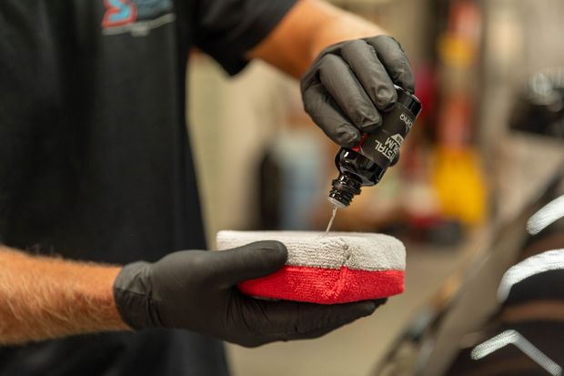 Gloved hands polishing a sneaker with a red-and-white sole using a small brush