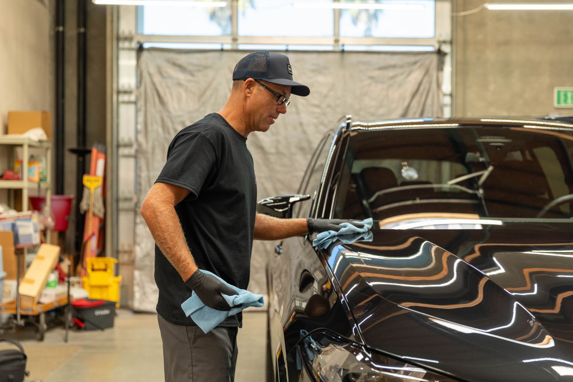 Technician in a black shirt and cap polishing a dark car in an auto shop
