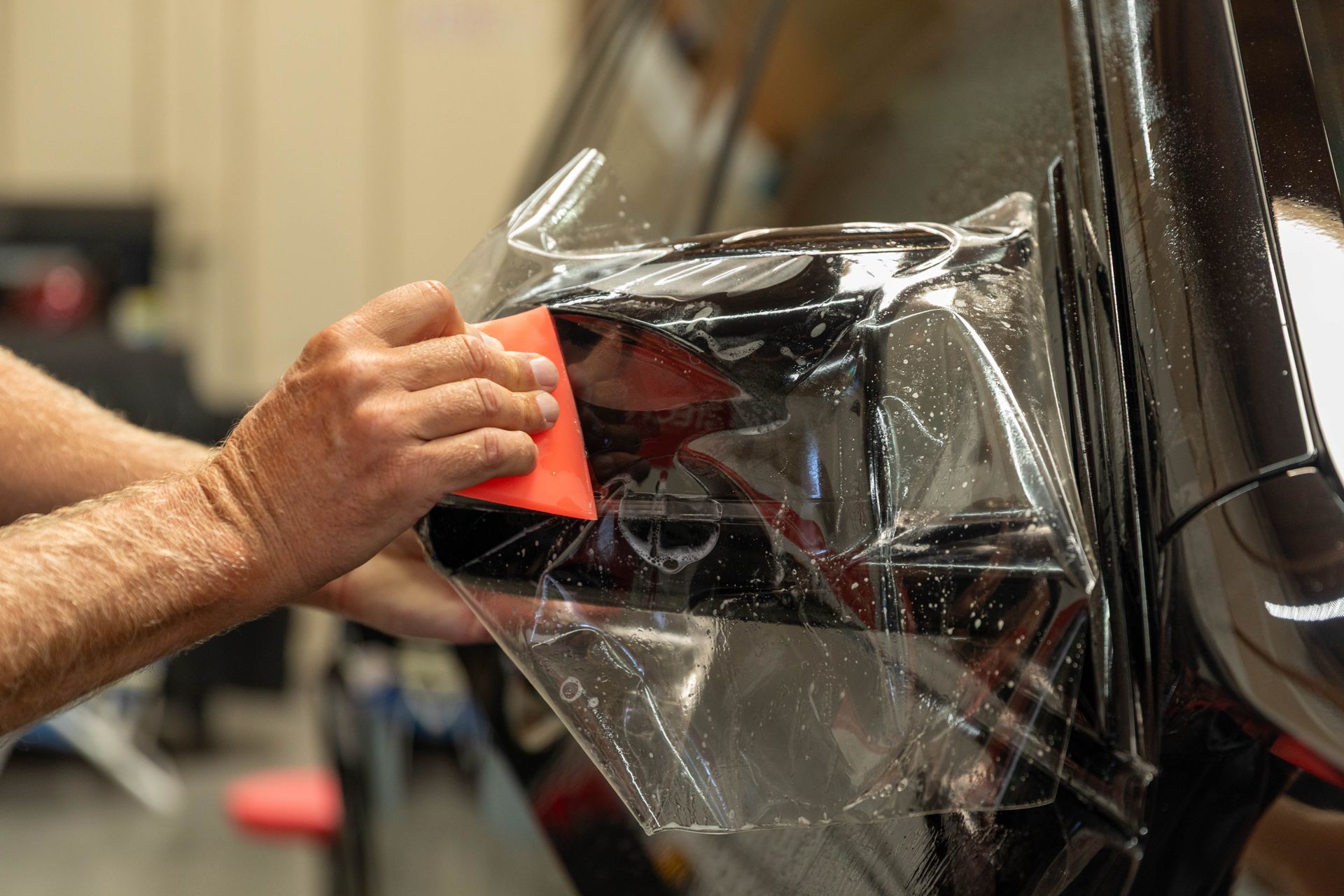Hand applying clear vinyl wrap to a black car panel with a red squeegee tool