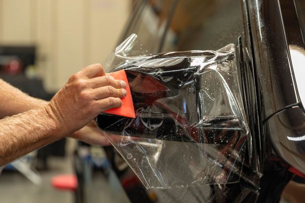 Hand applying clear vinyl wrap to a black car panel with a red squeegee tool