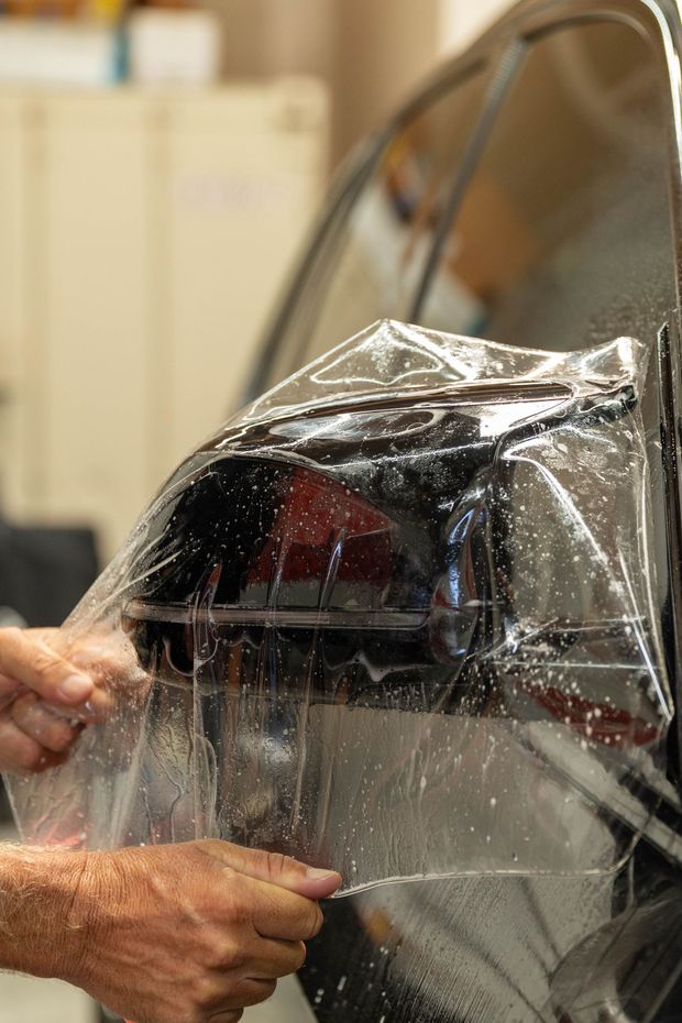 Person applying clear protective film to a car window