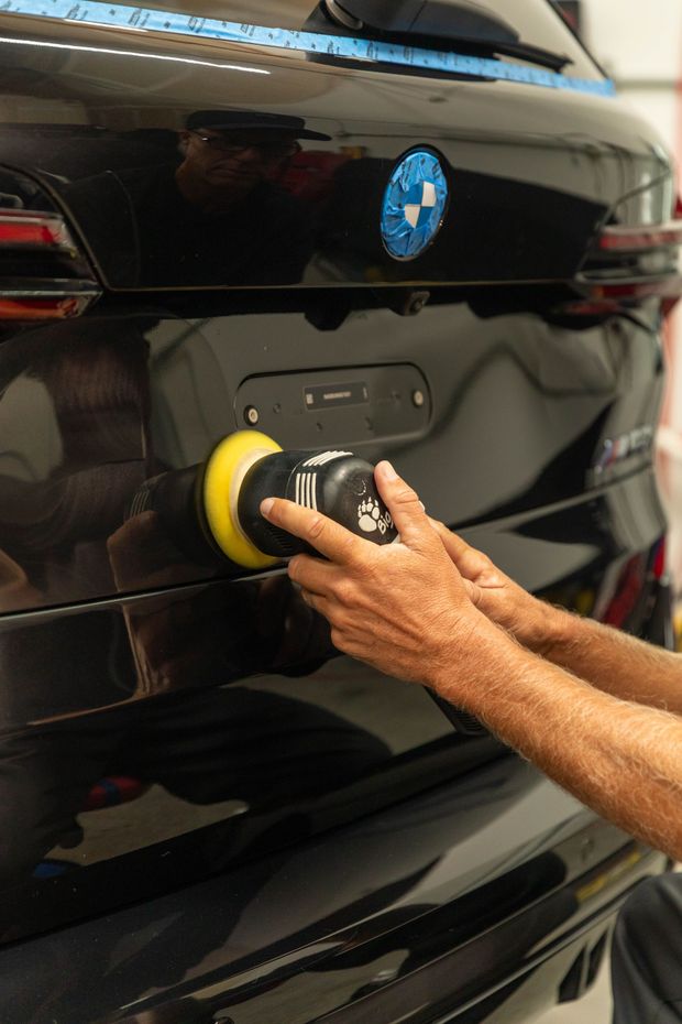 Hand polishing the glossy black rear of a BMW with a yellow buffing pad