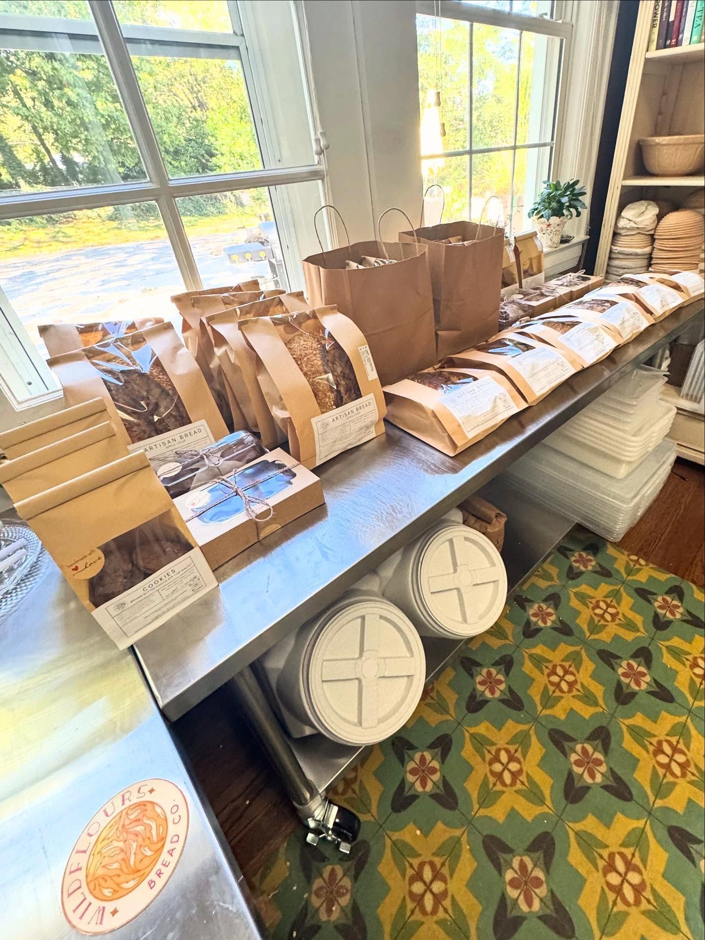 Counter with assorted paper bags and baked goods by a window in a cozy shop.