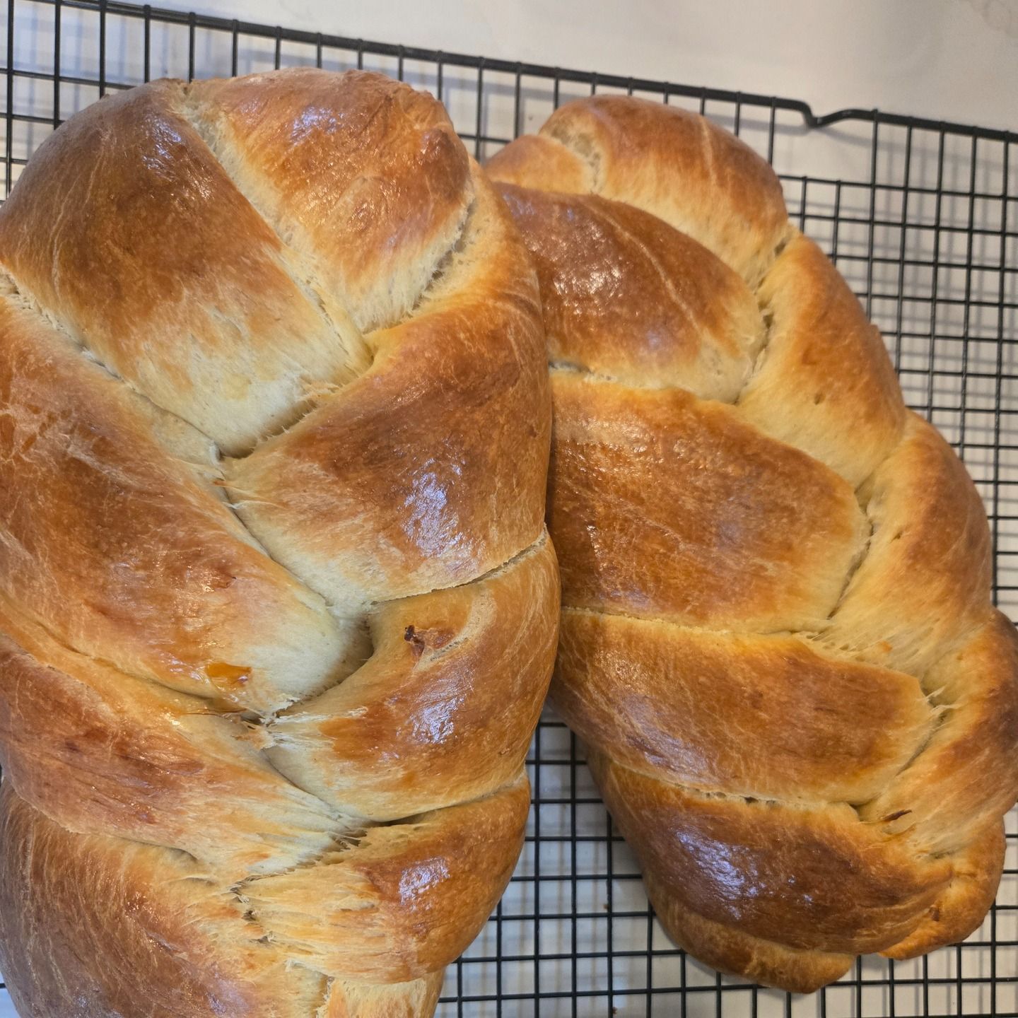 Two braided loaves of golden-brown bread cooling on a wire rack