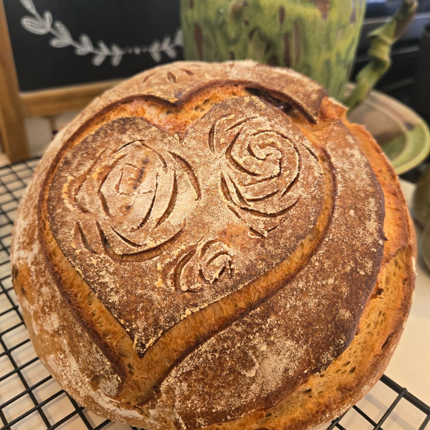 Round rustic loaf of bread with a heart and roses scored on top, cooling on a wire rack
