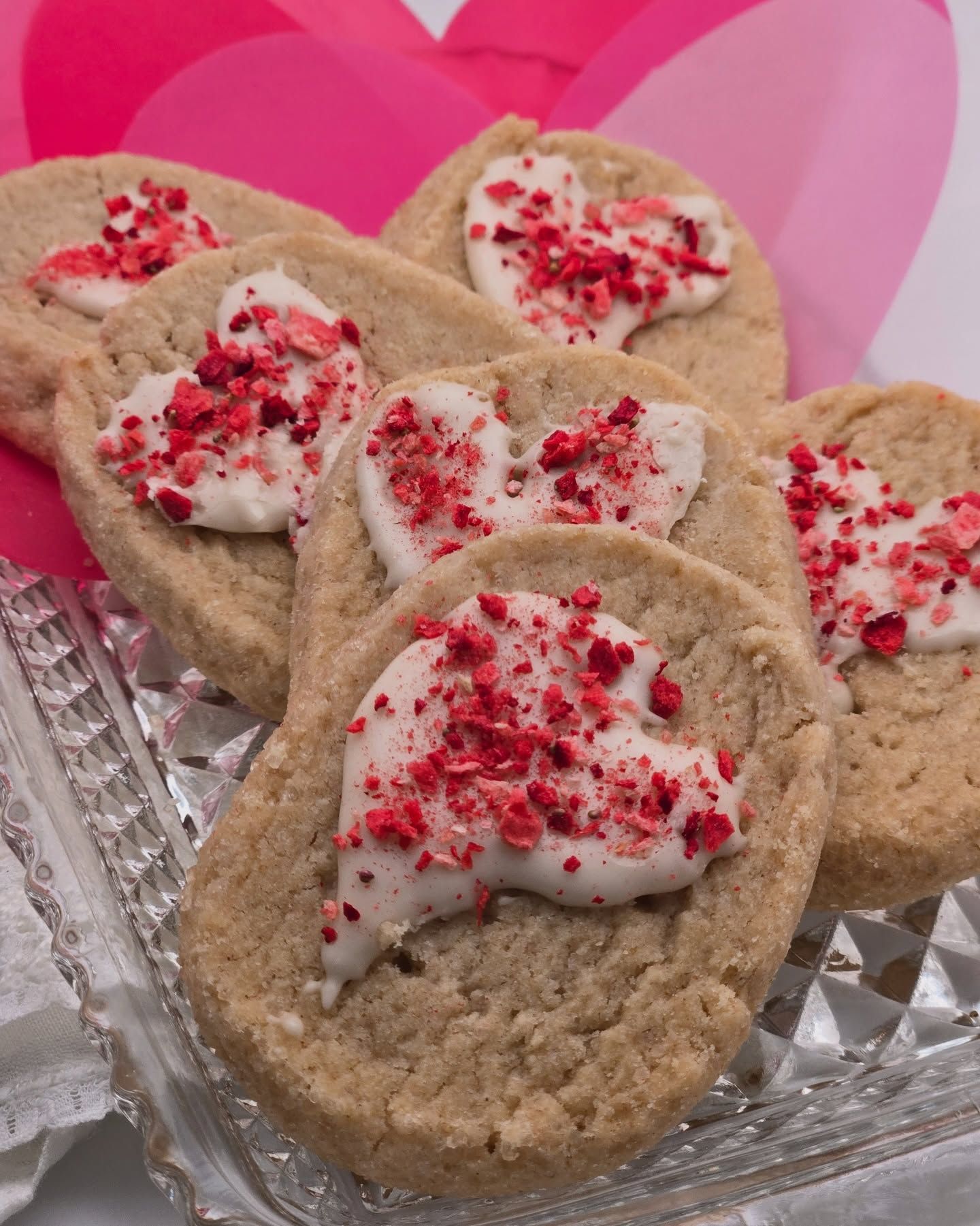 Close-up of heart-shaped cookies with white icing and red sprinkles on a glass tray