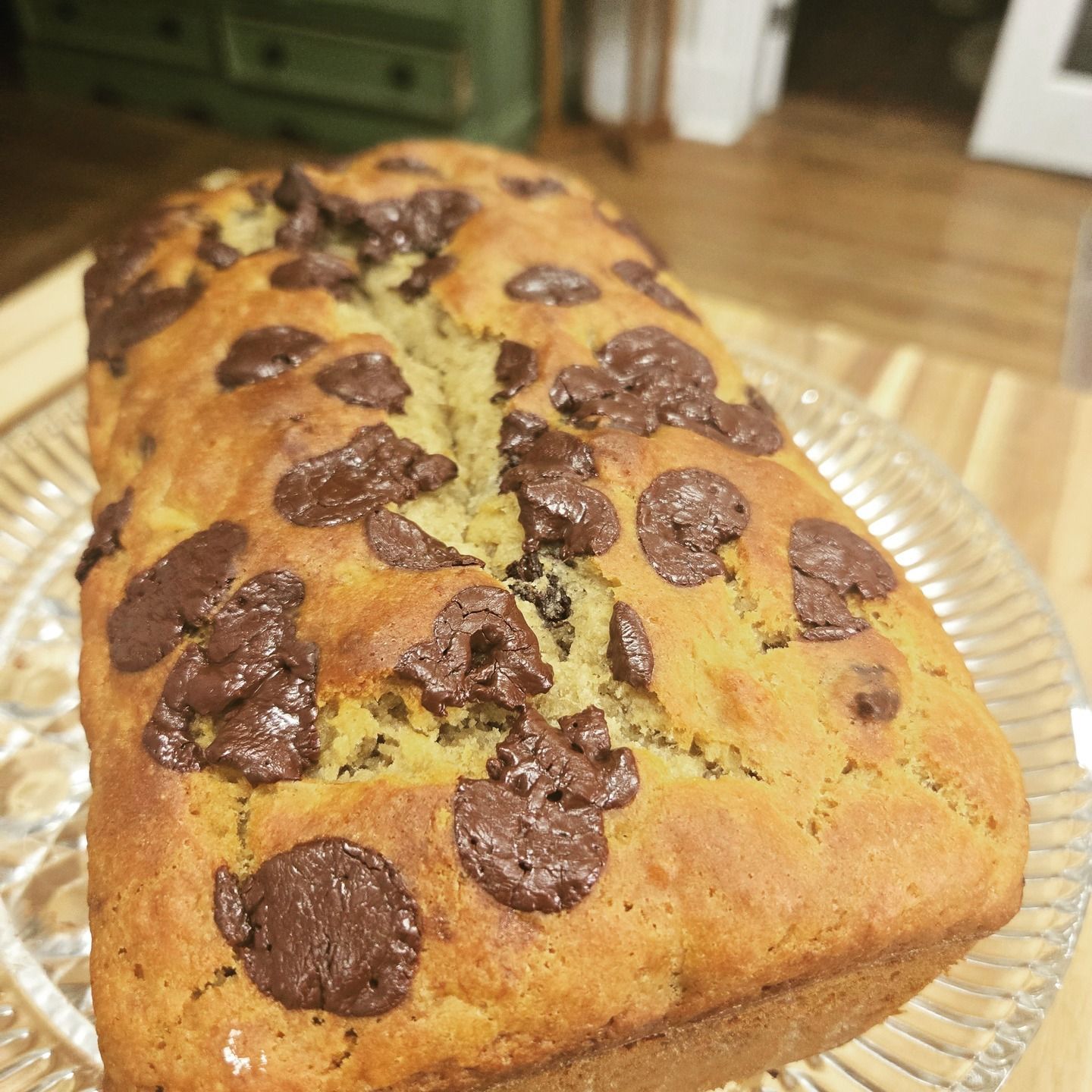 Chocolate chip loaf cake on a glass plate, with a golden crust and melted chocolate chunks on top