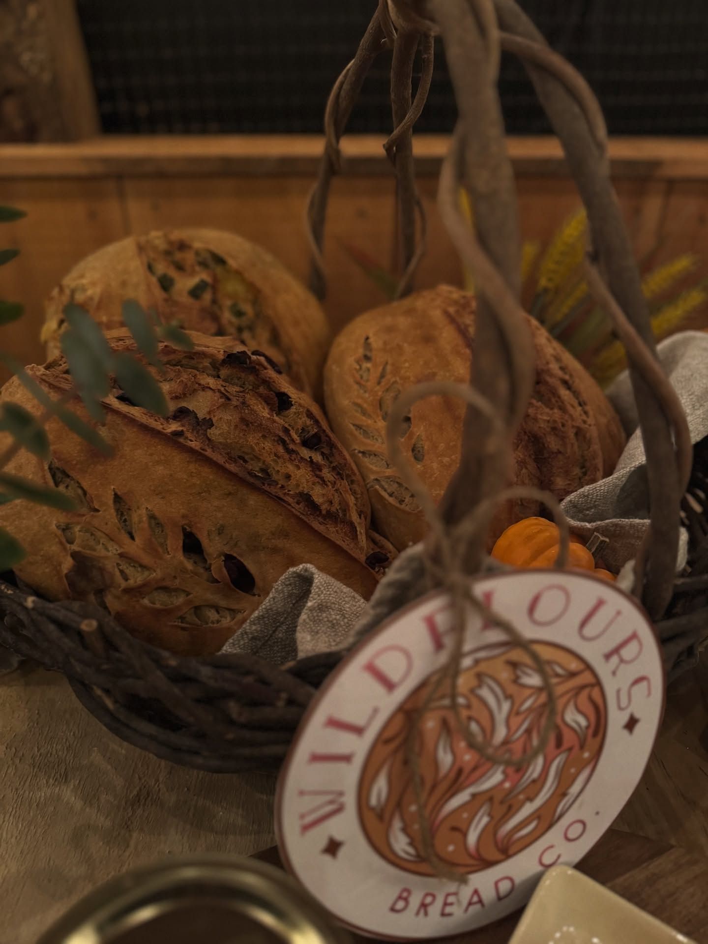 Rustic bread loaves in a basket with a “Wild Flour Bread Company” tag and dried orange slices