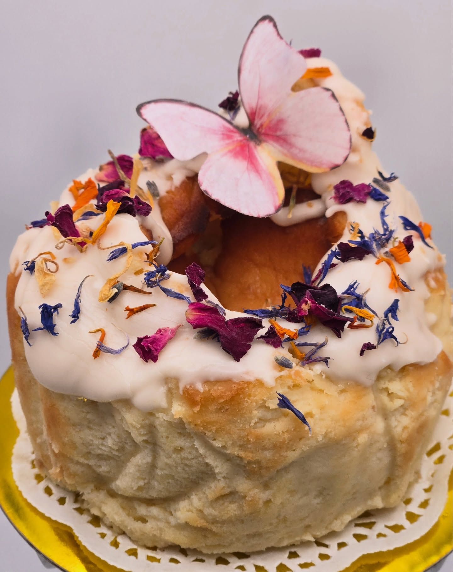 Flower-topped frosted pastry with colorful dried petals and a pink butterfly decoration