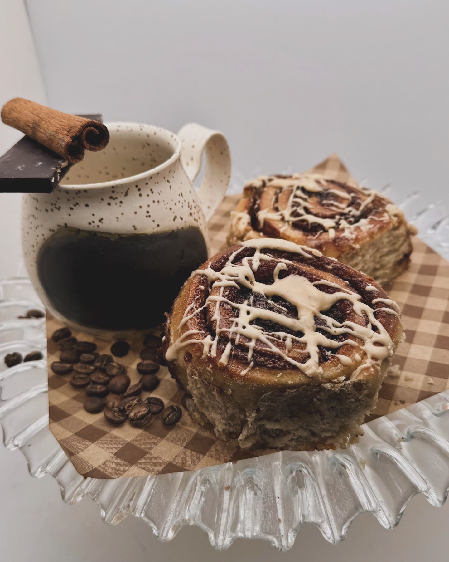Coffee mug with cinnamon stick and two iced pastries on a glass plate