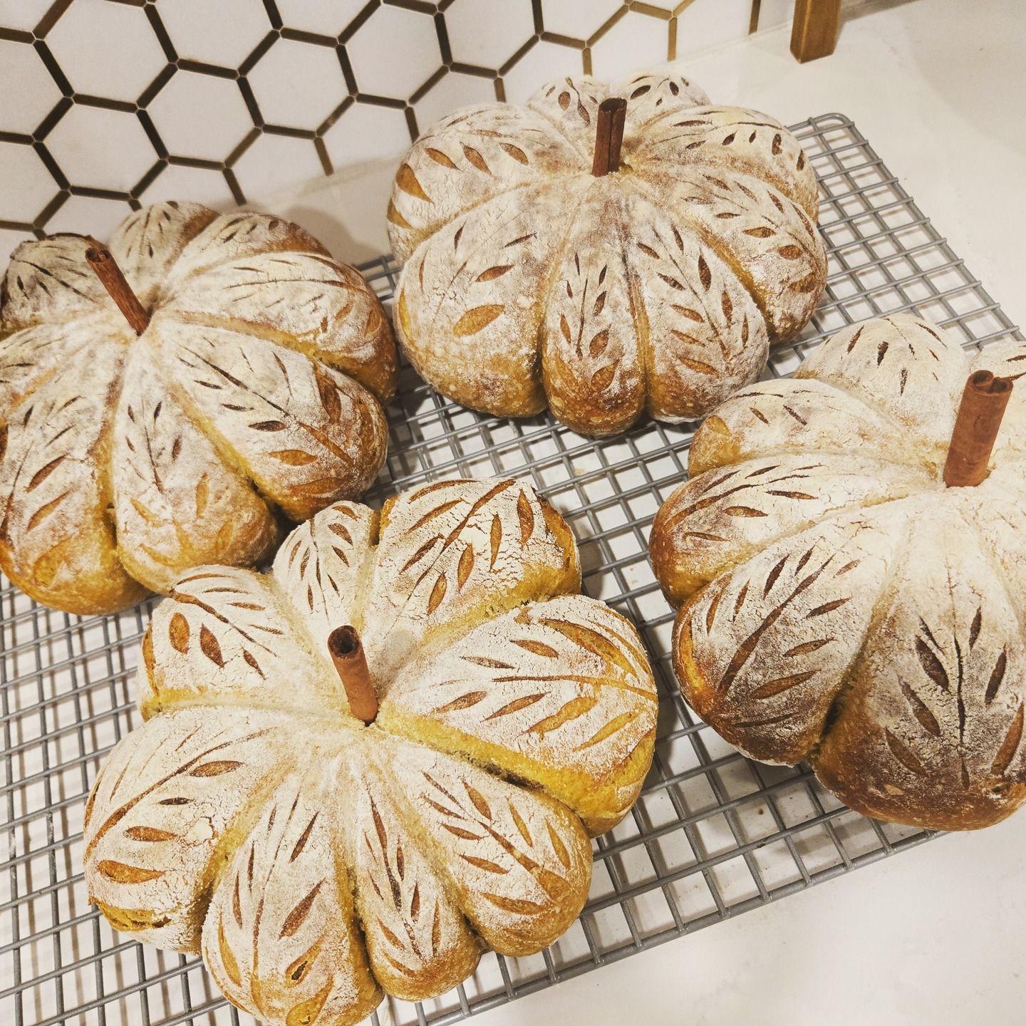 Four rustic pumpkin-shaped loaves on a cooling rack, dusted with flour and scored with leaf patterns.