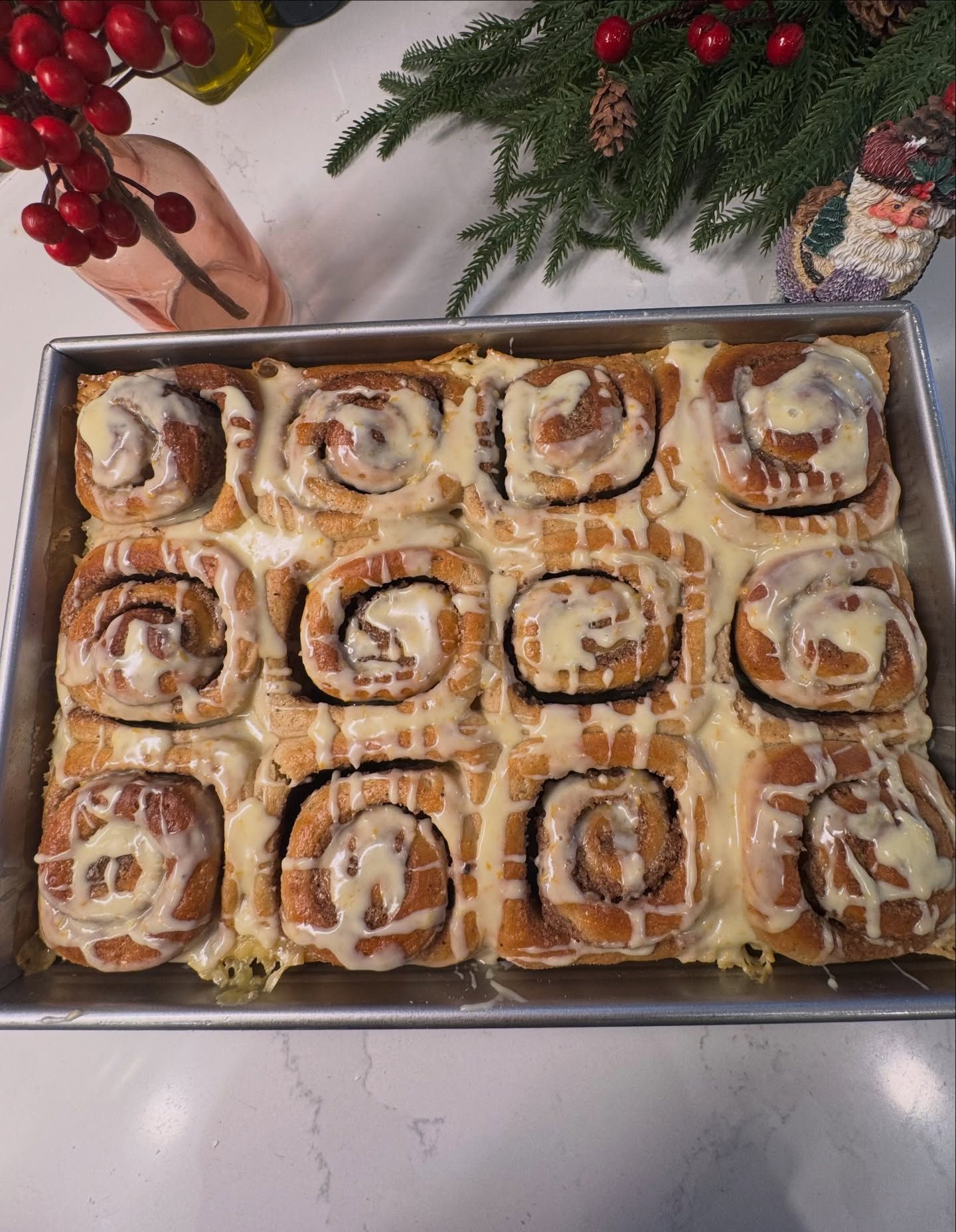 Tray of frosted cinnamon rolls on a kitchen counter with holiday greenery and red berries nearby