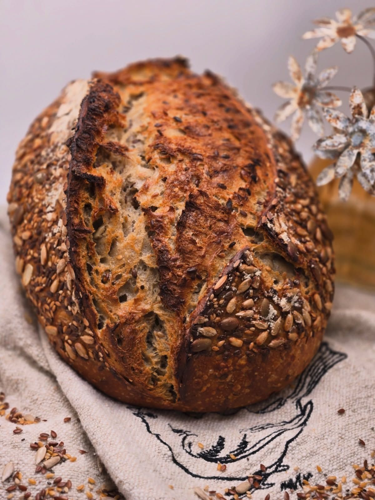 Rustic loaf of crusty bread on a linen cloth with dried flowers nearby