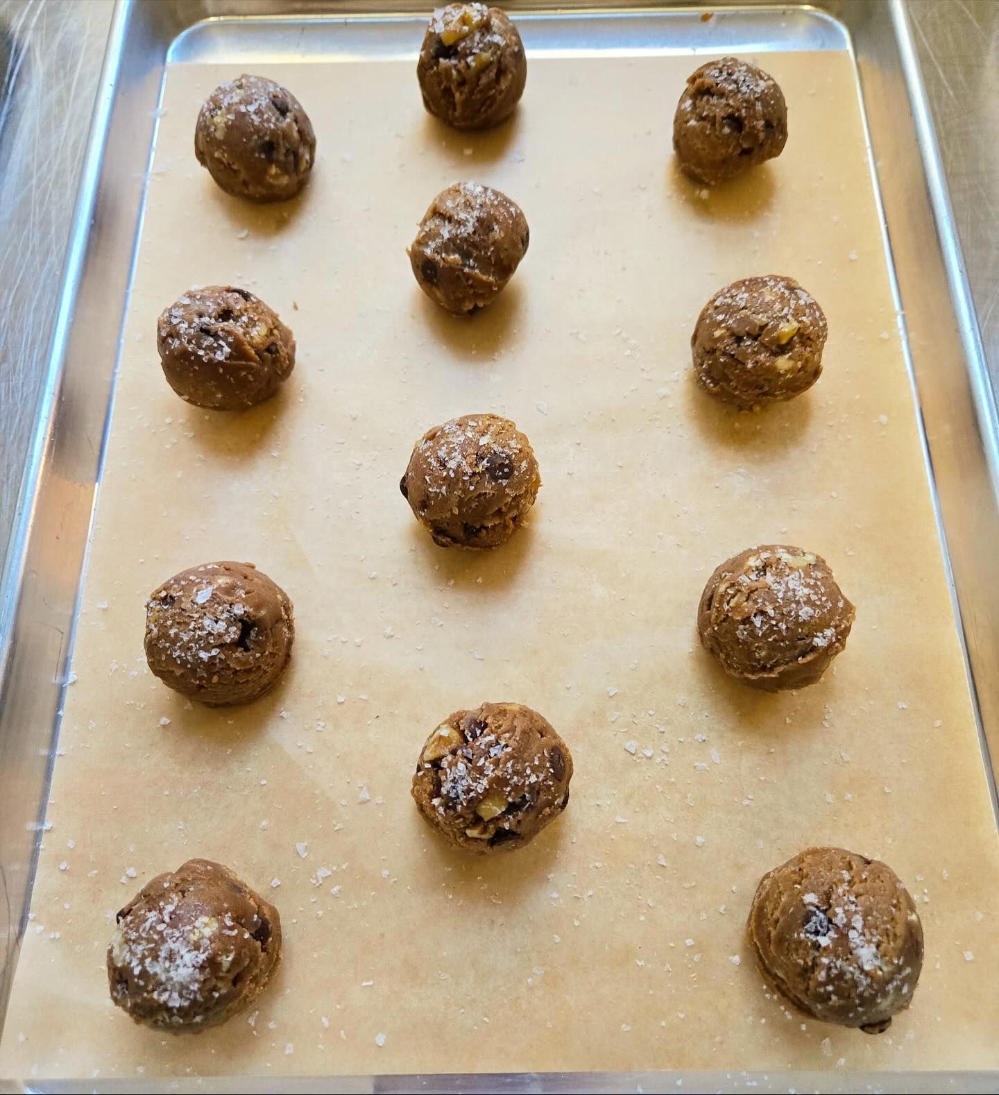 Twelve chocolate cookie dough balls spaced on a parchment-lined baking sheet