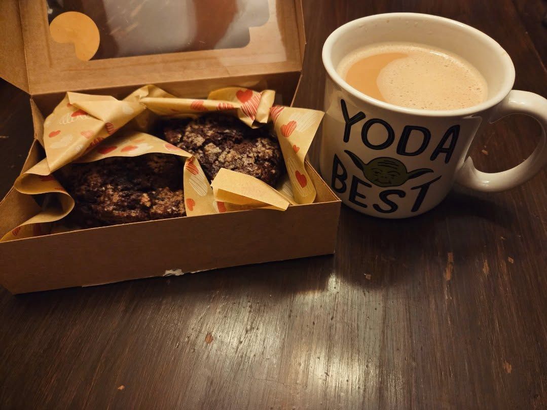 Donuts in a box beside a mug of coffee on a wooden table.