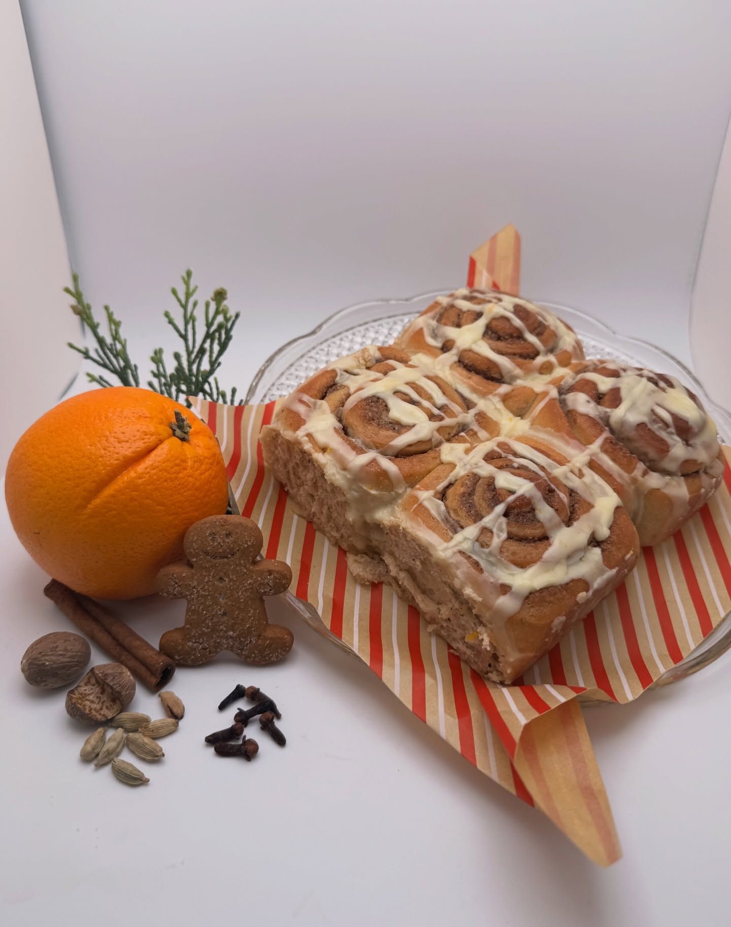 Orange and cinnamon bread loaf on a striped board, with an orange, spices, and sprigs beside it