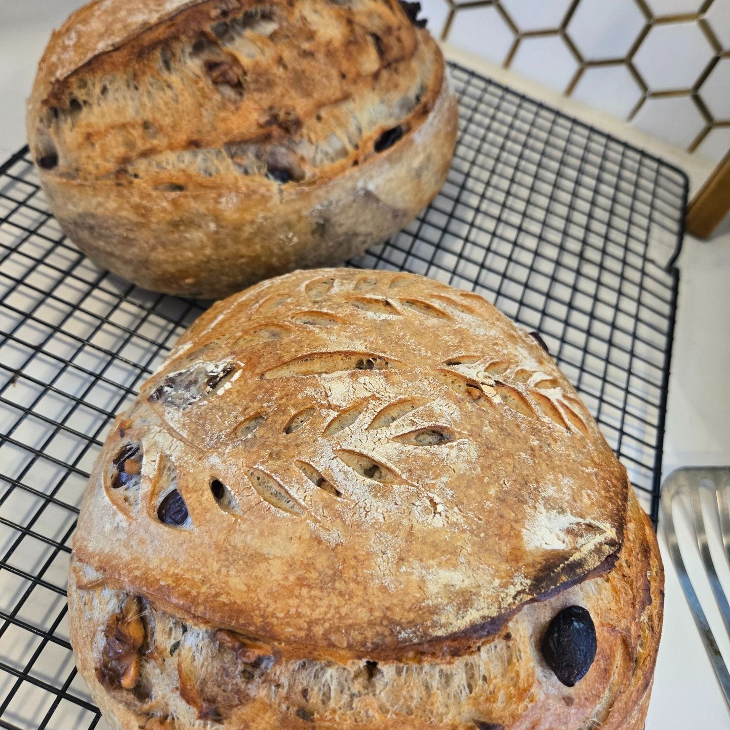 Two rustic loaves of bread cooling on a wire rack, one in front and one behind.