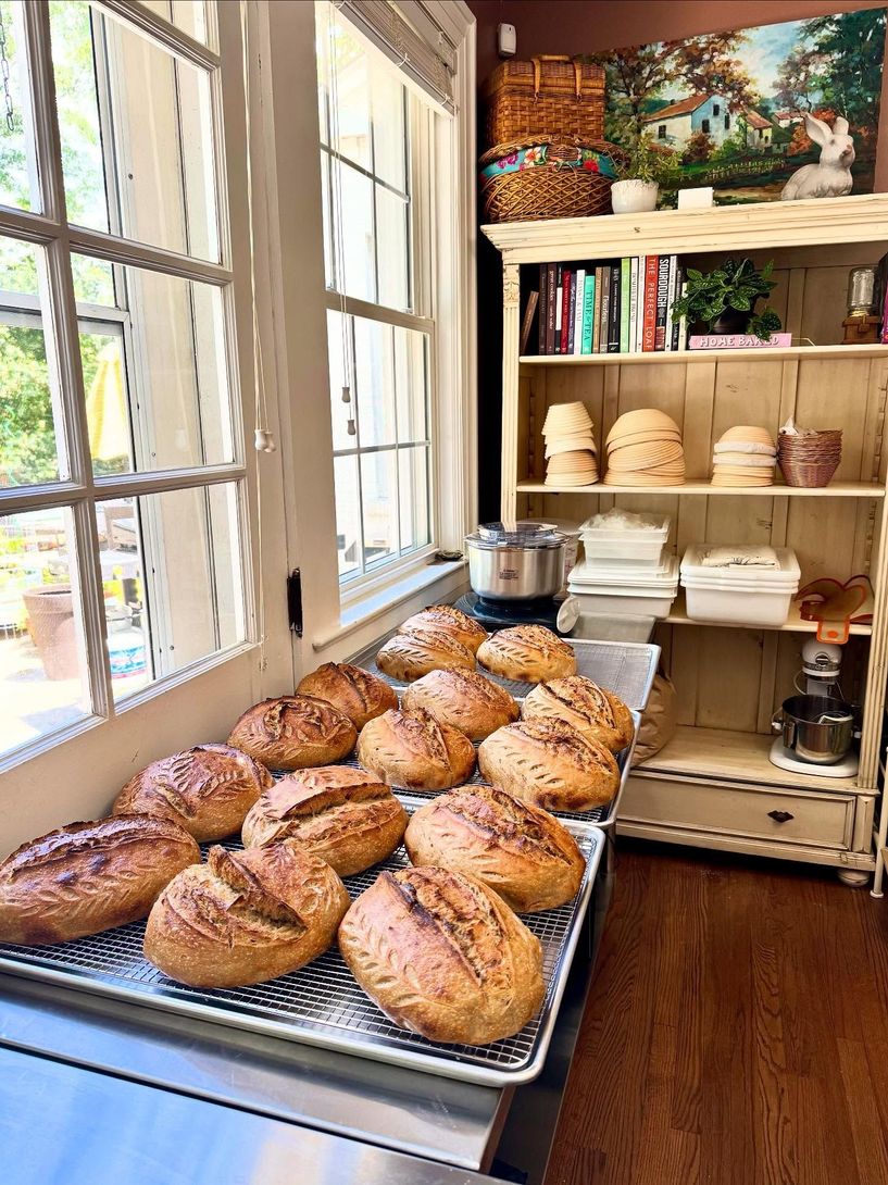 Tray of freshly baked loaves on a kitchen counter by a sunny window, with shelves of bread baskets nearby