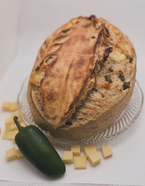 Crusty loaf bread with jalapeño pepper and cheese cubes on a white surface