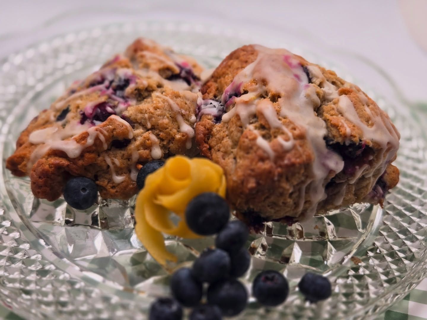 Blueberry scones with glaze on a glass plate, garnished with fresh blueberries and a flower-shaped fruit piece
