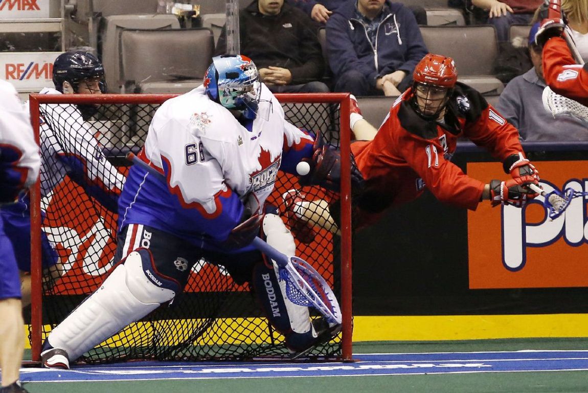 A hockey goalie is standing in front of a net holding a hockey stick.