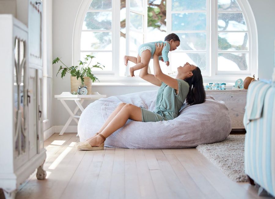 Mother lifting baby in a bright white nursery with large arched windows