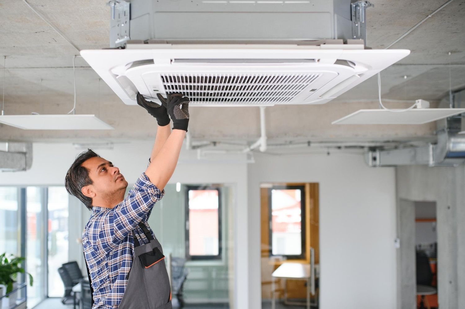Technician installing a ceiling cassette air conditioner in a room under construction
