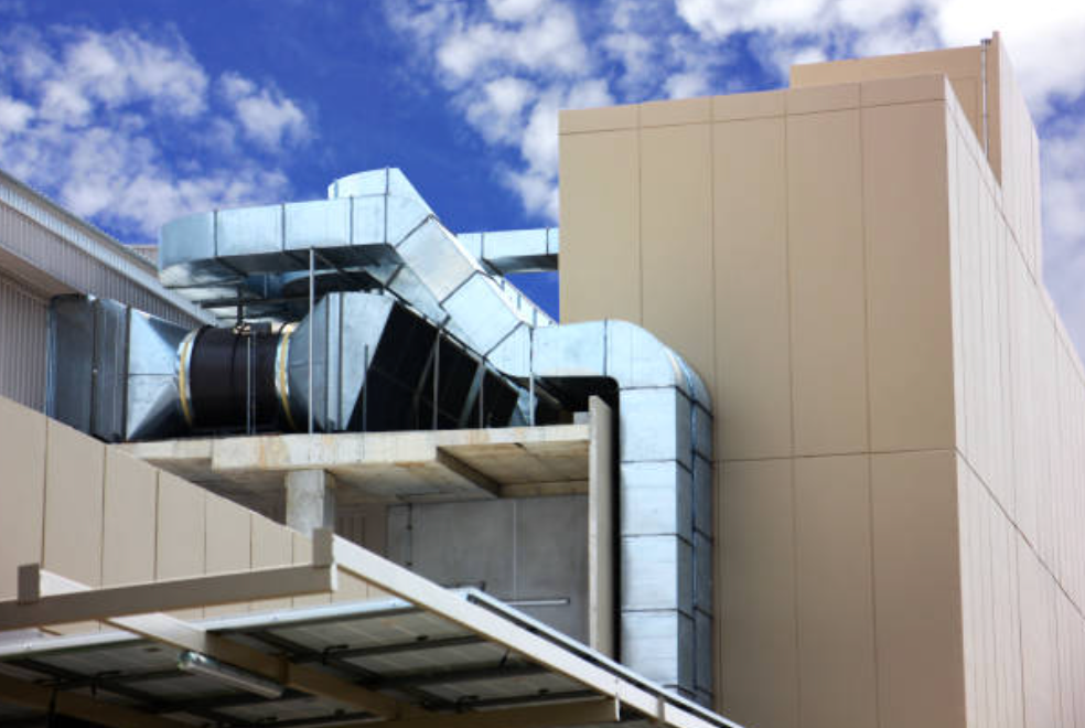 Rooftop HVAC ducts and beige building exterior against a blue sky with clouds
