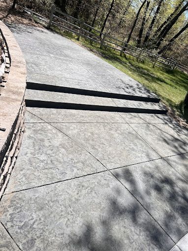 A concrete driveway with a stone wall and trees in the background.