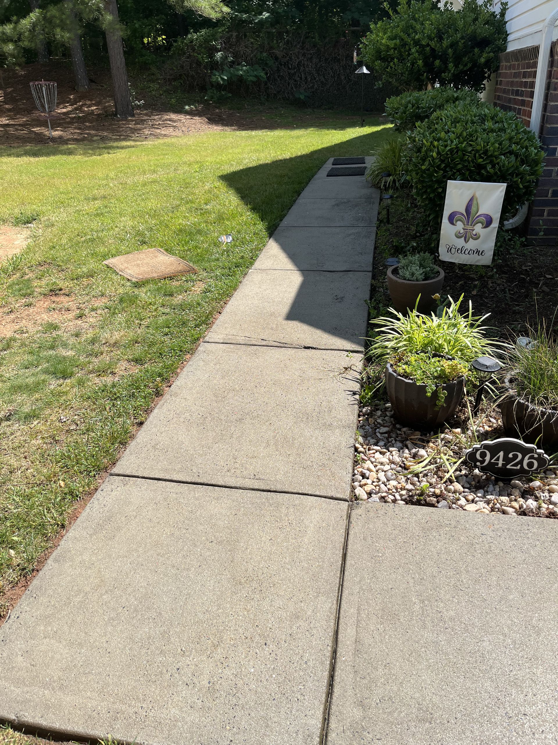 A sidewalk leading to a yard with a sign that says ' fleur de lis ' on it.