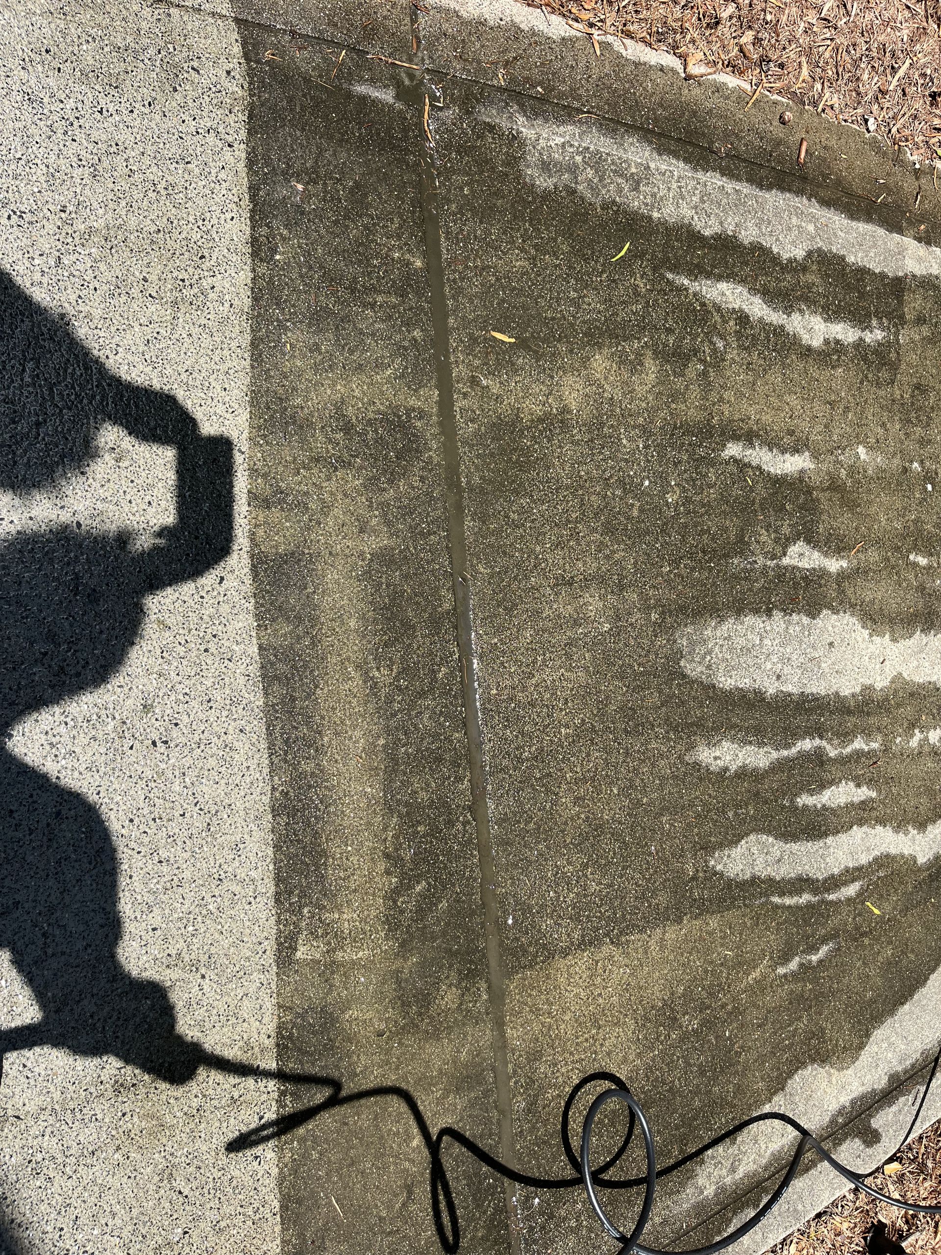 A person is using a pressure washer to clean a sidewalk.
