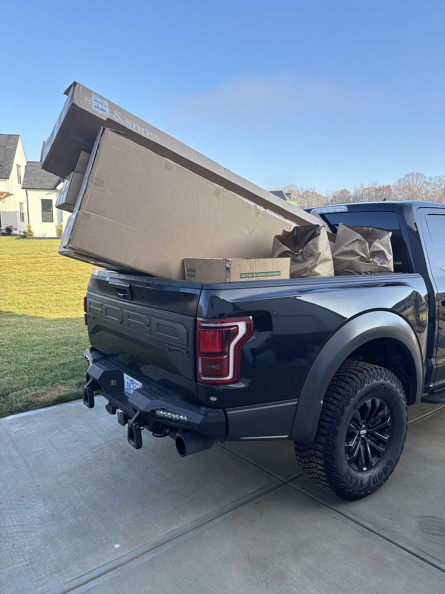 A black truck with boxes in the bed is parked in a driveway.