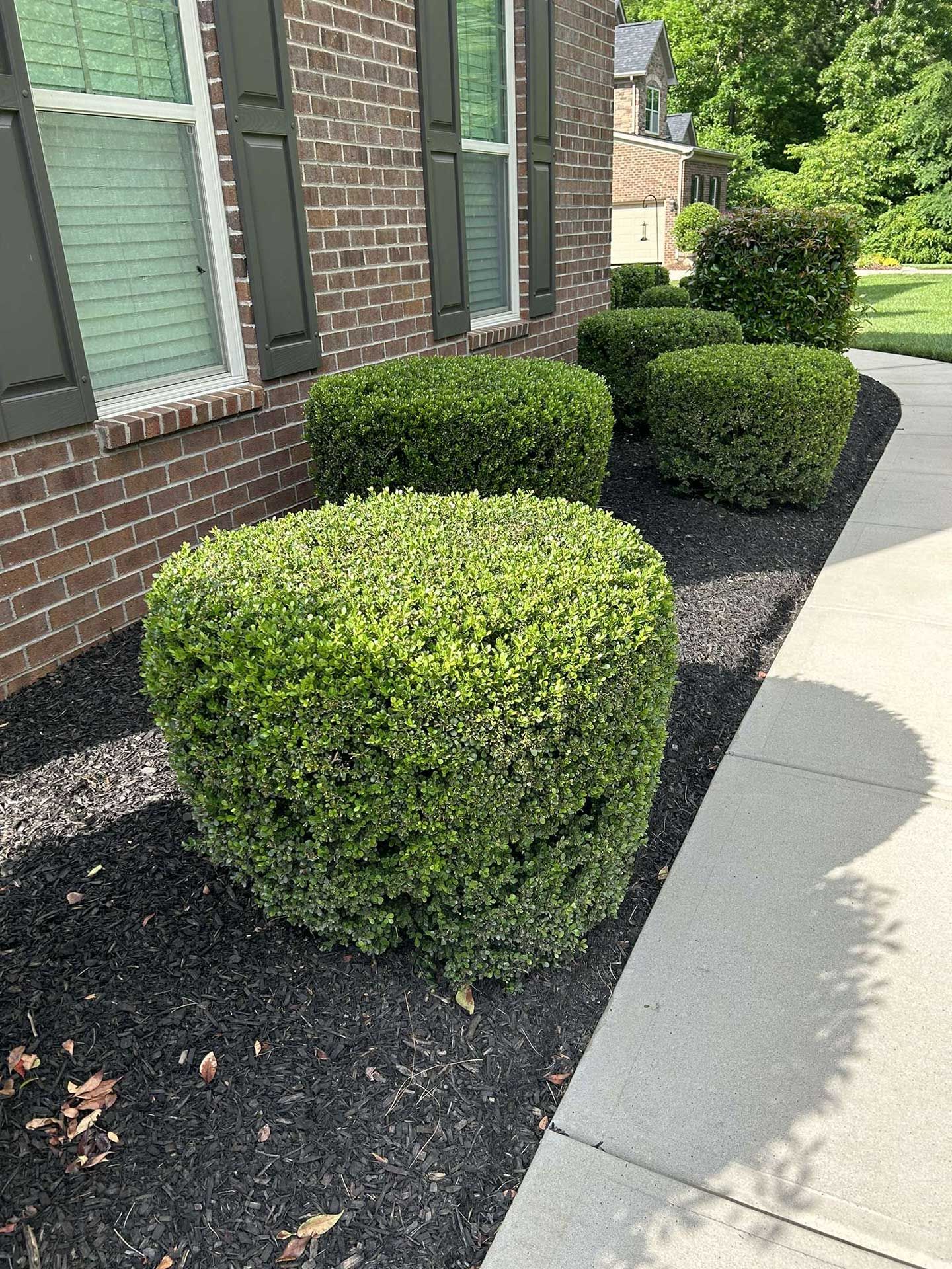 A brick house with a sidewalk and bushes in front of it.