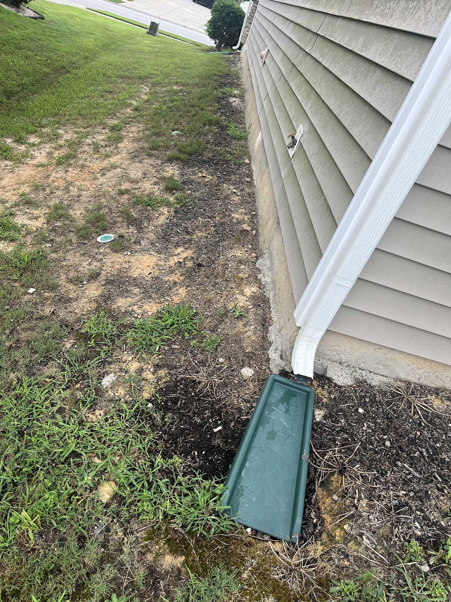 A gutter is sitting on the side of a house next to a hole in the ground.