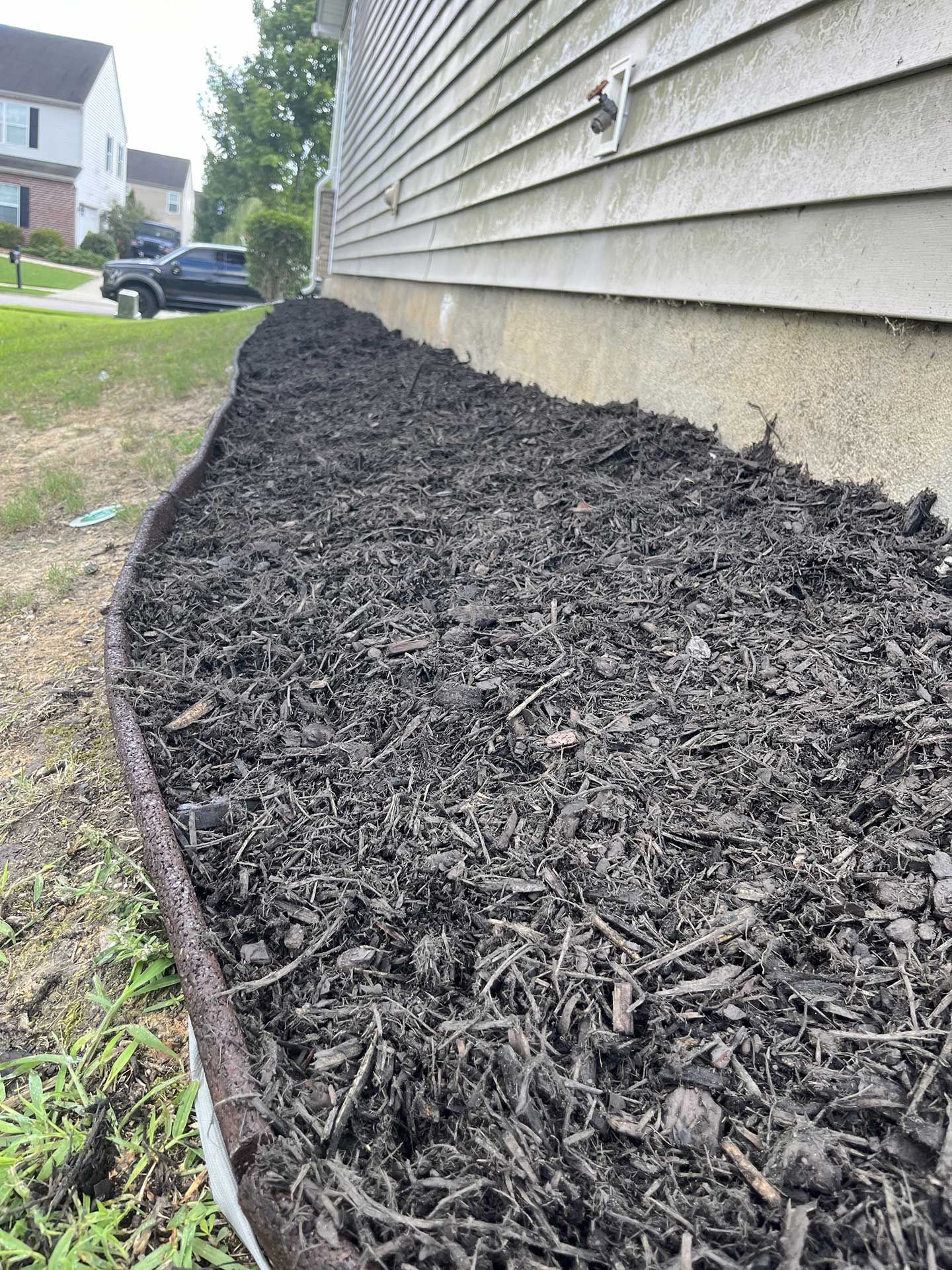 A sidewalk filled with black mulch next to a house.